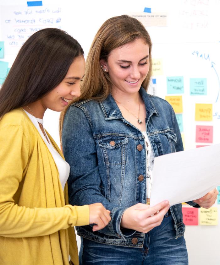 A photo of two women in front of a white board reading a document toge的r.